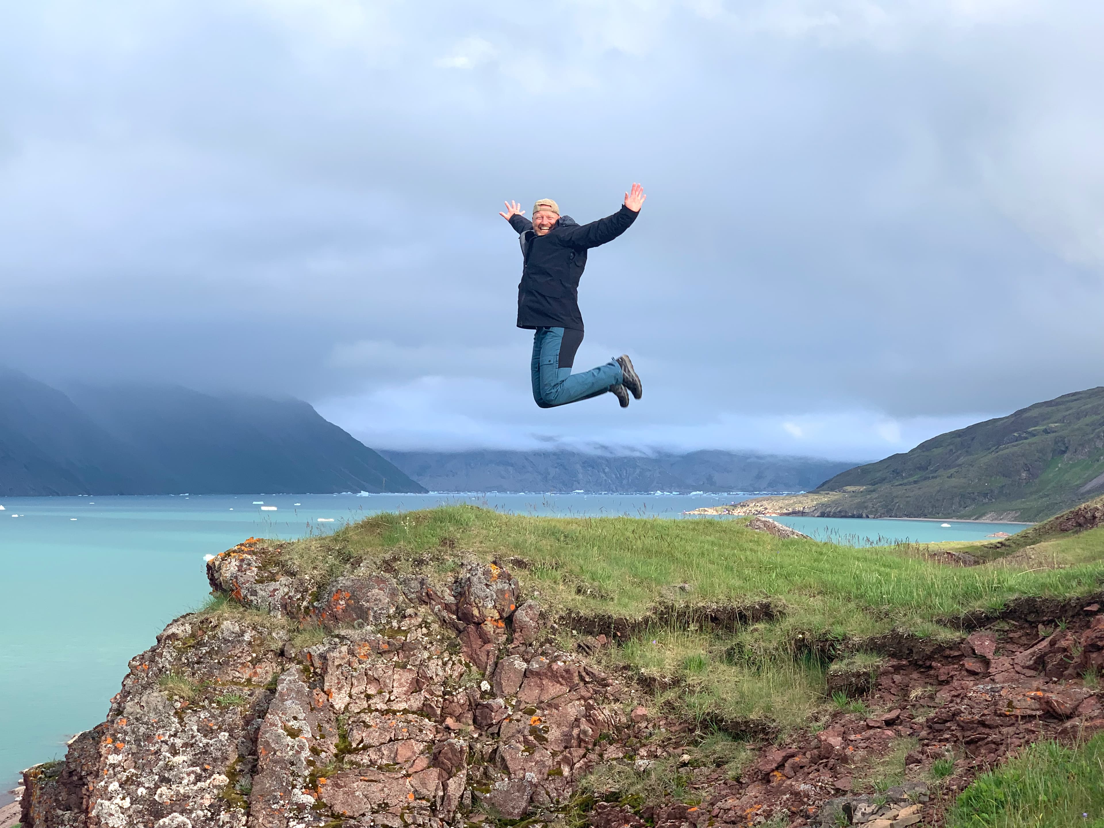 John Wehlast hoppende på Grønland, med bjerge i baggrunden